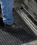 Person standing on Anti-Fatigue 3 Ft by 10 Ft Rubber Floor Mat for Commercial Kitchens with drainage holes and beveled edges