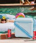Powder Blue 11 Qt Tag-Along Two Strapped Picnic Style Cooler With Hands Free Crossbody Strap beside a pool and drinks