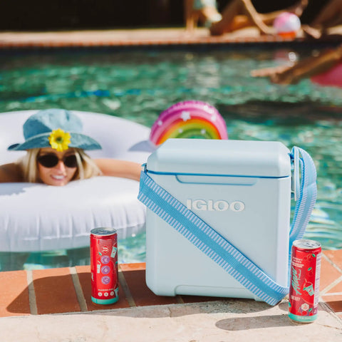 Powder Blue 11 Qt Tag-Along Two Strapped Picnic Style Cooler With Hands Free Crossbody Strap beside a pool and drinks