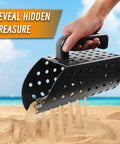 Hand using Workhorse Heavy Duty Sand Scoop For Metal Detecting With Shovel And Trowel Beach Sand Sifter, black plastic perforated scoop on beach