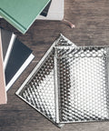 Metallic Bubble Mailers 75 Pack 6 By 9 Inch Padded Envelopes with Self Seal Foil Bags for mailing, shipping on wooden desk.