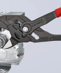 Heavy Duty 10 Inch Pliers Wrench With Adjustable Smooth Jaws grips a metallic pipe fitting in a workshop setting.