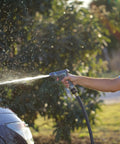 Person using a garden hose with brass garden hose quick connect fitting on a sunny day, spraying water on a car outdoors.
