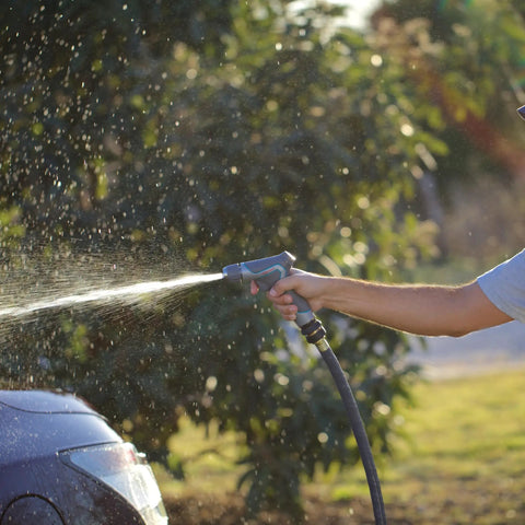 Person using a garden hose with brass garden hose quick connect fitting on a sunny day, spraying water on a car outdoors.