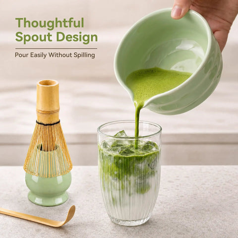 Complete Five Piece Matcha Making Kit With Bamboo Whisk, ceramic bowl pouring matcha into glass, whisk holder nearby