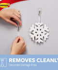Hands using Damage Free Hanging Wall Hooks For Small Decor Clear Wire Toggle Hooks With Adhesive Strips to hang a snowflake.