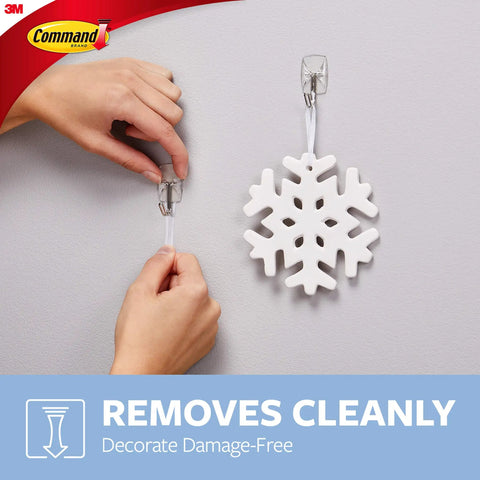 Hands using Damage Free Hanging Wall Hooks For Small Decor Clear Wire Toggle Hooks With Adhesive Strips to hang a snowflake.