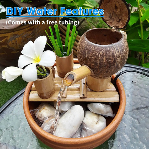 DIY water feature setup with bamboo and coconut components, flowing water into a stone-filled basin, plumeria flower displayed.