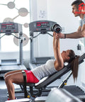 Woman on a bench press assisting with dumbbells in a gym setting, wearing Universal Belt Squat Collar For Nordic Hamstring Curl On Bench