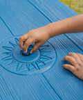 Child's hand on Sun And Fun Picnic Table With Umbrella For Indoor And Outdoor Use Toddler Sized Table With Five Foot Shade Canopy That Blocks UVA And UVB Rays For Safe Chill Backyard Fun