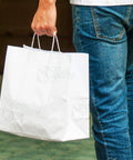 Person holding large white kraft paper bags with handles 13x7x17 inches 200 count durable reusable shopping gift bags go to party retail merchandise lunch and grocery use eco friendly packaging.