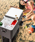 Portable Patio Cooler Bar Cart 80QT Rolling Beverage Station with ice and drinks on beach with people, dark gray rattan.