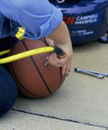 Person using 17 Piece Compressor Inflation Kit With Blow Gun, Air Chucks And Inflation Needles to inflate a basketball outdoors.
