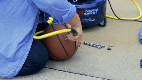 Person using 17 Piece Compressor Inflation Kit With Blow Gun, Air Chucks And Inflation Needles to inflate a basketball outdoors.