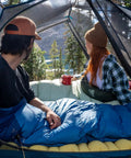 Campers in tent using Cosmic 20 Down Mummy Sleeping Bag With 550 Fill Power Down, Recycled Fabrics And PFAS Free DWR, 2024 Model