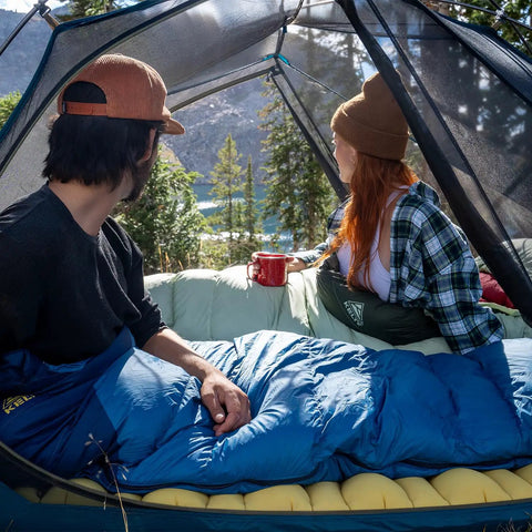 Campers in tent using Cosmic 20 Down Mummy Sleeping Bag With 550 Fill Power Down, Recycled Fabrics And PFAS Free DWR, 2024 Model