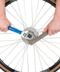 All In One Chain Whip And Pedal Wrench For Bike Maintenance, 10.75 Inch Steel Tool, being used on a bicycle wheel cassette