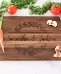 Wooden cutting board laser-engraved with personalized names Samantha & Jackson and year 2021, decorative leafy wreath
