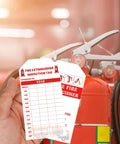 Hand holding 100 Pcs Monthly Fire Extinguisher Inspection Tags With Clear Readable Records near fire extinguisher