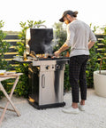 Outdoor gas grill with man cooking on stainless steel grill in a backyard.