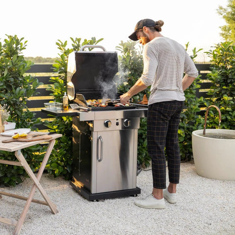 Outdoor gas grill with man cooking on stainless steel grill in a backyard.