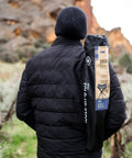 Person outdoors with Apex Fold-Up Stool G-140 Black Grey Ultra Portable Camp Seat on shoulder, red rock backdrop