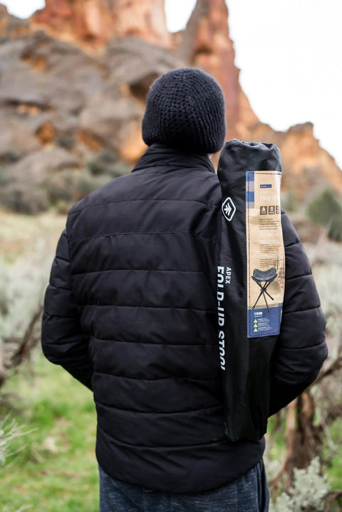 Person outdoors with Apex Fold-Up Stool G-140 Black Grey Ultra Portable Camp Seat on shoulder, red rock backdrop