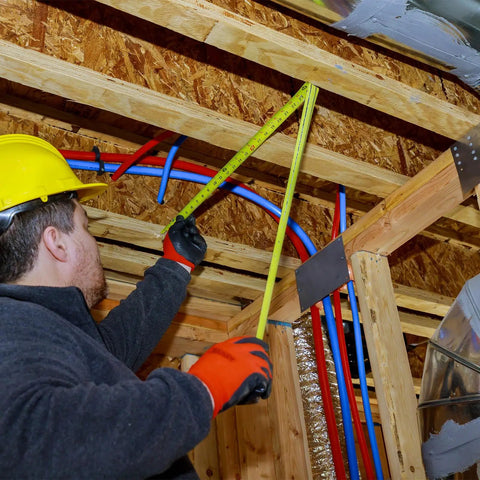 Person measuring pipe installation with a measuring tape in a home renovation setting using Meccanixity Steel Spring Pipe Bender for 1 Inch PVC Tube.