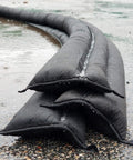 Stacked water activated 5 foot sandless flood barrier 4 pack self-inflating absorbs water and rises to form a tight barrier for quick flood control black for home and business flood prep and emergency readiness on wet pavement