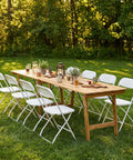 Folding Chairs Set Of 20 With 330 Lb Capacity, Plastic Stackable Chairs arranged around an outdoor wooden table in a garden setting.