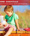 Atickyaid mini first aid kit red pouch with white cross; child seated outdoors while knee is bandaged.