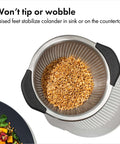 Top view of Non Slip Grip 5 Qt Stainless Steel Colander with Comfortable Handles containing grains, showing durable nesting strainer.