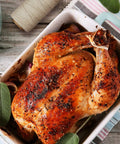 Roasted chicken tied with beige 1mm 3-ply butchers twine cotton cooking string in casserole, with twine spool nearby