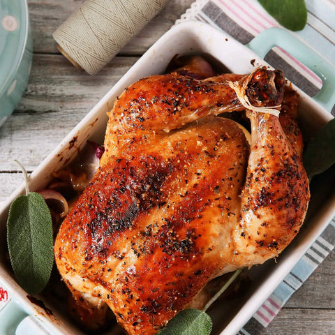 Roasted chicken tied with beige 1mm 3-ply butchers twine cotton cooking string in casserole, with twine spool nearby