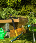 Four Pack 15 Inch Mattock Hoe With Steel Forged Pickaxe And Fiberglass Handle Built For Weeding Prospecting Camping And Hand Digging This All Purpose Workhorse Tool Set in garden next to plants and wheelbarrow
