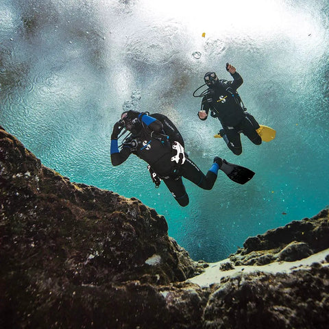 Two divers using Donut Wing For Technical Scuba Diving With Inflator Hose And K Style BPI 40 Lbs 18 Kg Capacity Black Ultra Durable 1000D Cordura Outer Shell And 500D Inner Bladder Eco Friendly Dope Dyed Fabric For Abrasion Resistance underwater near rocks