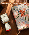 Monthly Date Stamp Set With Weather Icons And Calendar Stamps For Planners Easy Peasy Organizer Craft Supplies Hella Convenient Number Trackers That Make Daily Planning A Total Breeze Without Any Stress Or Trouble on a wooden table with a floral scrapbooking journal.