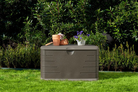Beefy 73 Gallon Resin Outdoor Storage Deck Box Weather Resistant Brown in garden setting with plants on top