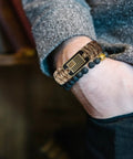 Paracord Bracelet For Men Tactical Survival Gear With Bronze USA Flag Charm on wrist, adjustable fit, green camo style.