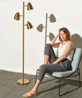 Tall LED Floor Lamp With Adjustable 3 Light Tree In Antique Brass Gold Finish next to a seated woman in a modern living room