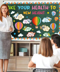 Teacher presenting Hot Air Balloon Healthy Bulletin Board Set For Classroom Decor With Colorful Cutouts And Borders 73 Piece Kit Includes Healthy Habits Cutouts Take Your Health To New Height Letters Clouds Stars And Borders For Back To School Chalkboard Wall to students in classroom.