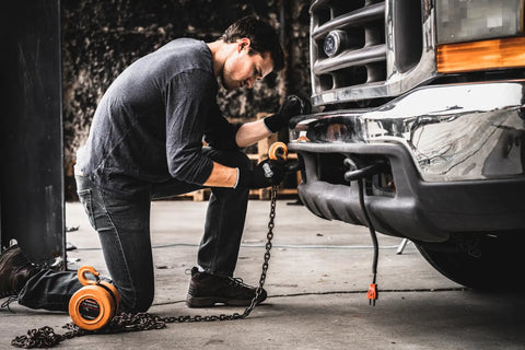 Man wearing Never Slip Maximum Grip All Purpose Work Gloves For Men In Wet Dry And Oily Conditions With Polymer Palm Black Blue Extra Large Size 15 Pairs Durable Construction All Weather Ready, connecting a chain to a vehicle.