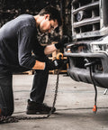 Man kneeling, wearing Never Slip Maximum Grip Work Gloves for Men with Polymer Palm Coating, adjusting chains on a truck.