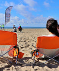 Two orange foldable beach chairs with cup holders on sand, Low Profile Beach Chair Set Of 2 For Adults And Kids, seaside view.