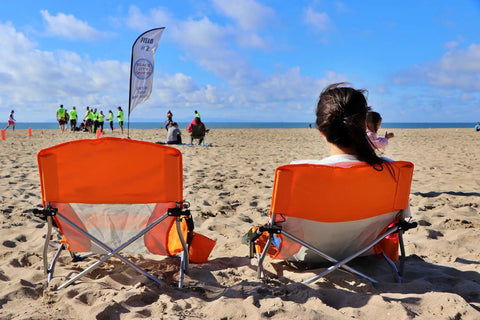 Two orange foldable beach chairs with cup holders on sand, Low Profile Beach Chair Set Of 2 For Adults And Kids, seaside view.