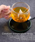 Electric Mug Warmer And Cooler For Desk keeps tea at 55°C on a black thermal pad, held in hand, ideal for focused work.