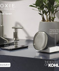 Moxie Alexa Enabled Showerhead With Dope Bluetooth Speaker and Radio next to sink, charging on dock, polished chrome finish