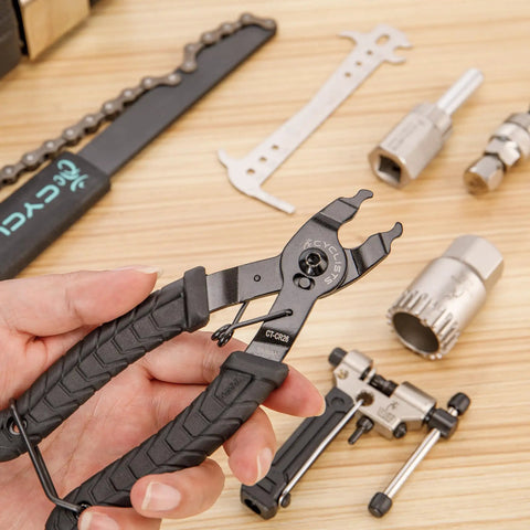 Detail of 7 Piece Bike Tool Kit With Storage Case For Mountain And Road Bikes, including chain rivet extractor and pliers on wood surface
