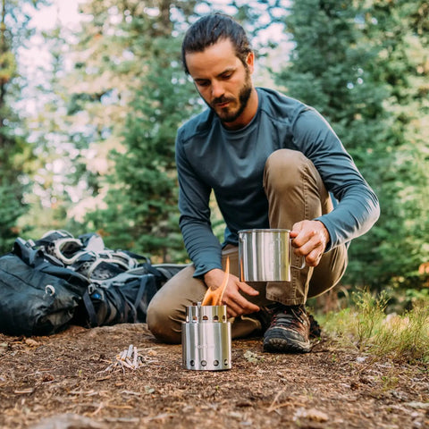 Camper using Lite Pot 900 Wood Burning Camp Stove Set With 900 Milliliter Pot in forest, showcasing compact design.