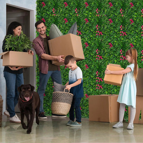 Family with boxes and dog in front of Boxwood Faux Grass Wall Panels 12 Pack 20x20 Inch Dense Green Backdrop For Indoor Outdoor Privacy Screen And Dope Green Wall Decor For Garden Backyard Patio And Balcony.
